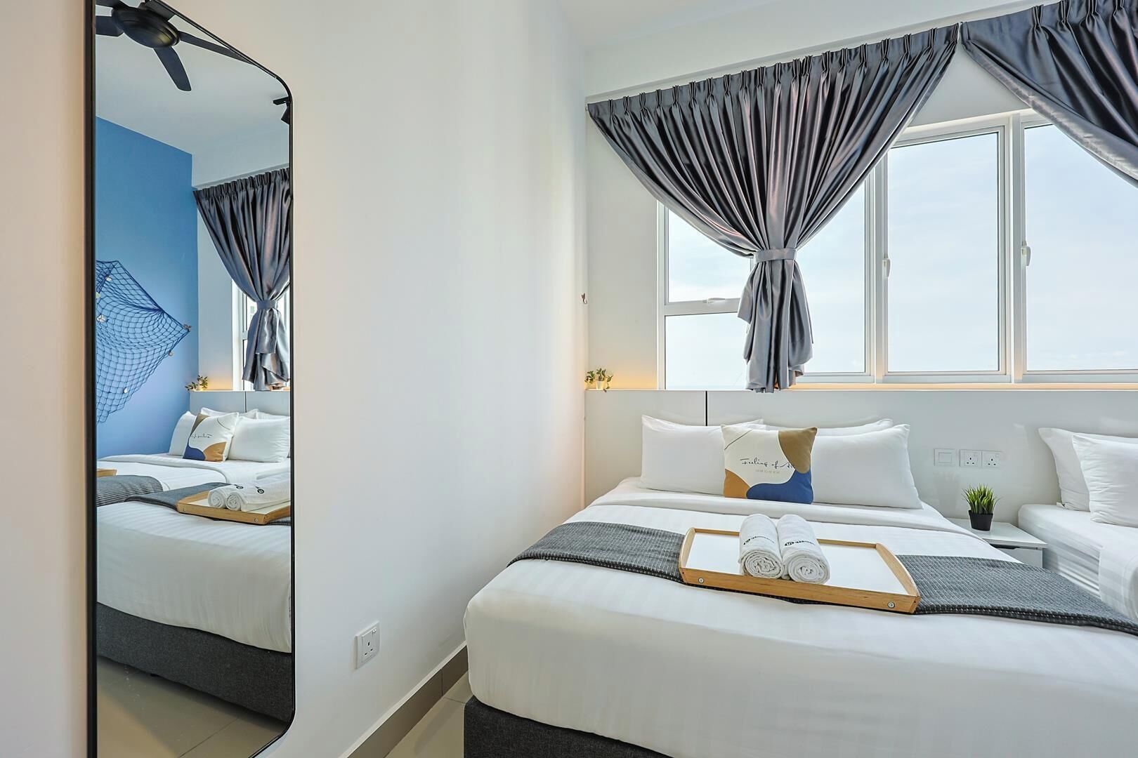 Habitación de hotel con cama, espejo, ventana con cortinas y vista al cielo.