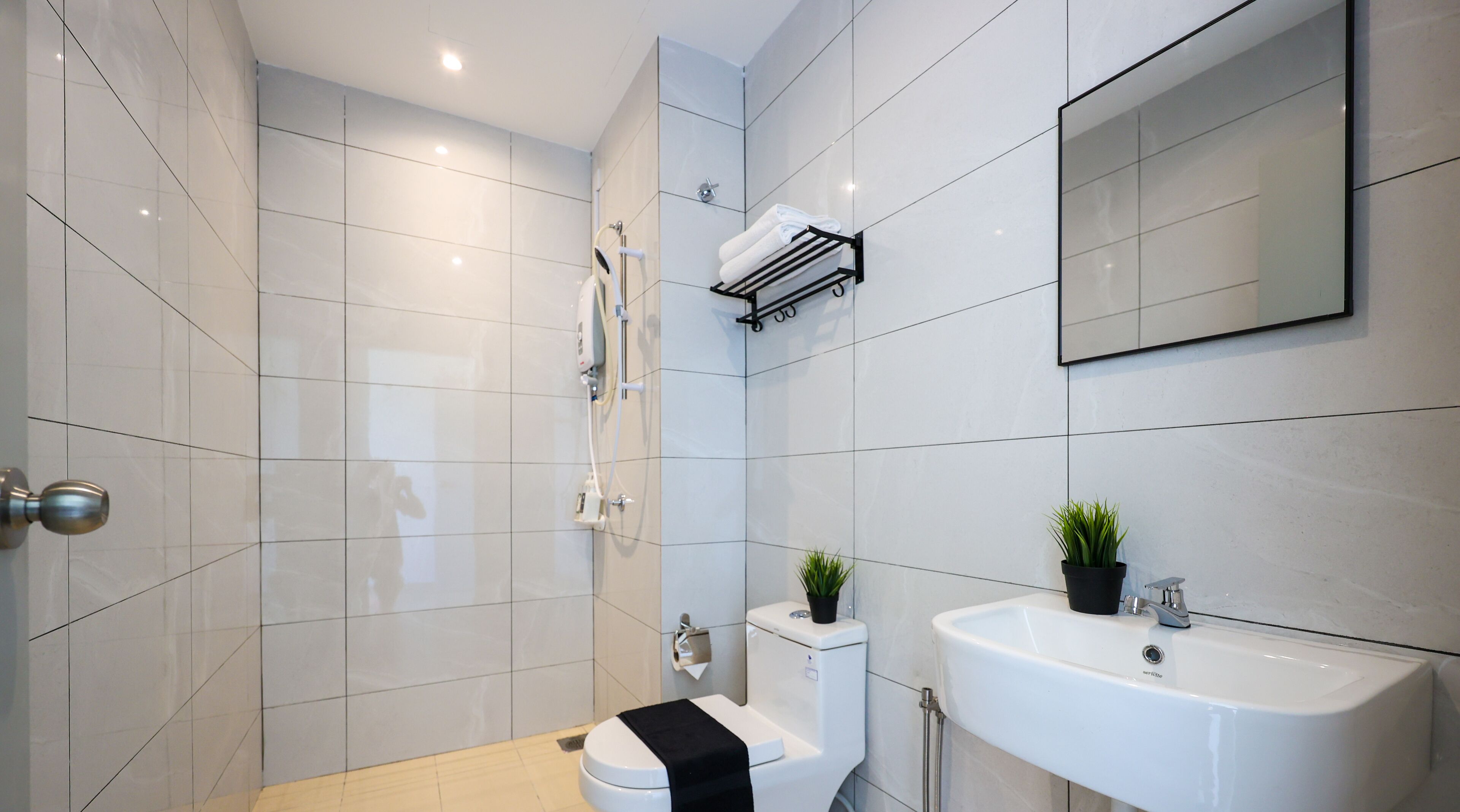A modern bathroom with white tiles, a toilet, a sink, a shower, and a mirror.