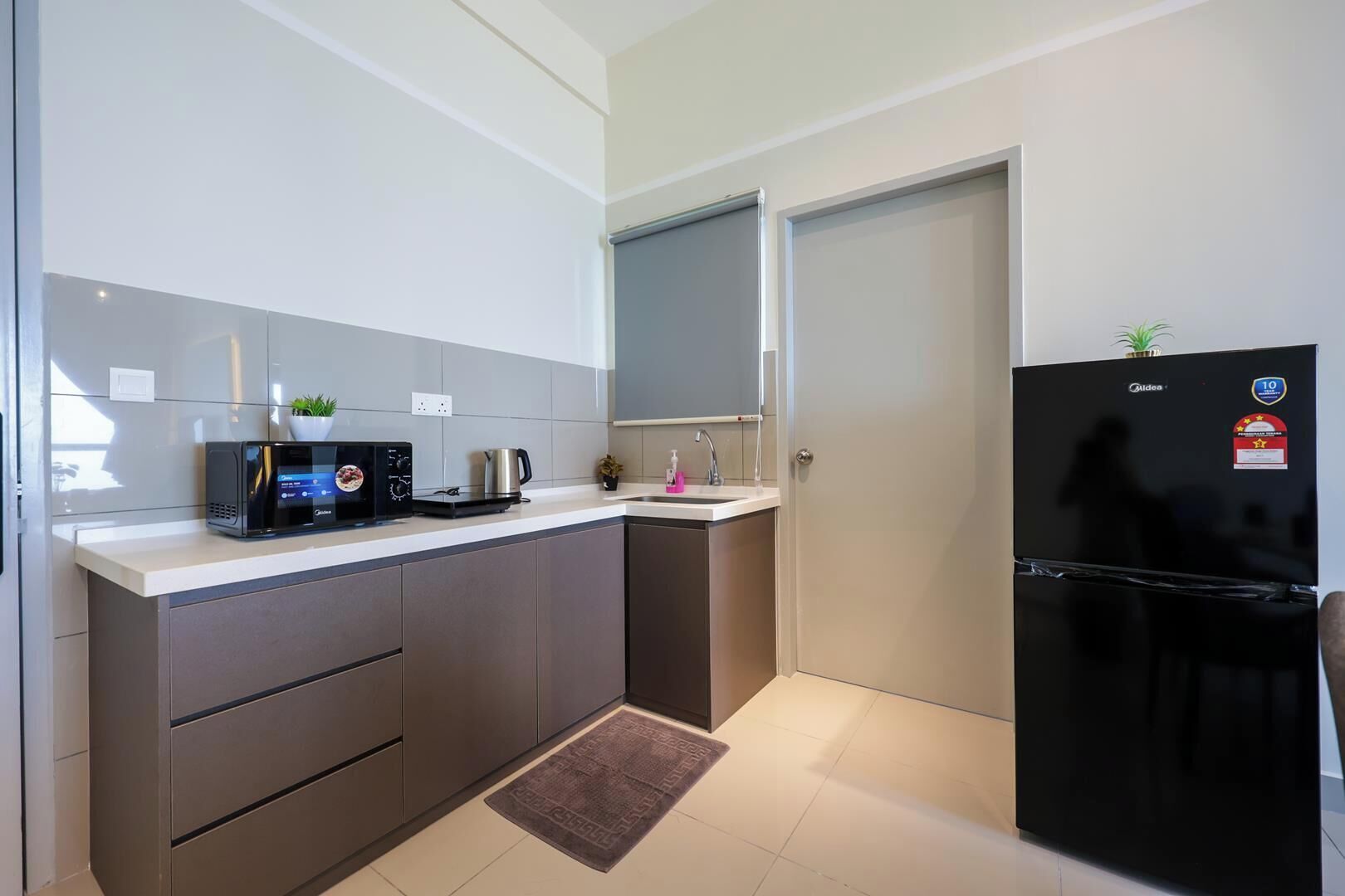 A compact kitchen with a microwave, kettle, and a refrigerator.