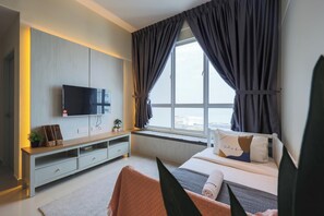 A modern bedroom with a TV mounted on the wall, a bedside table, a bed with pillows, a window with curtains, and a view outside.