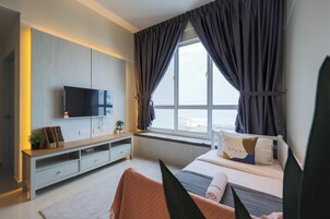 Una camera da letto moderna con una TV a muro, un comodino, un letto con cuscini, una finestra con tende e vista all'esterno.
