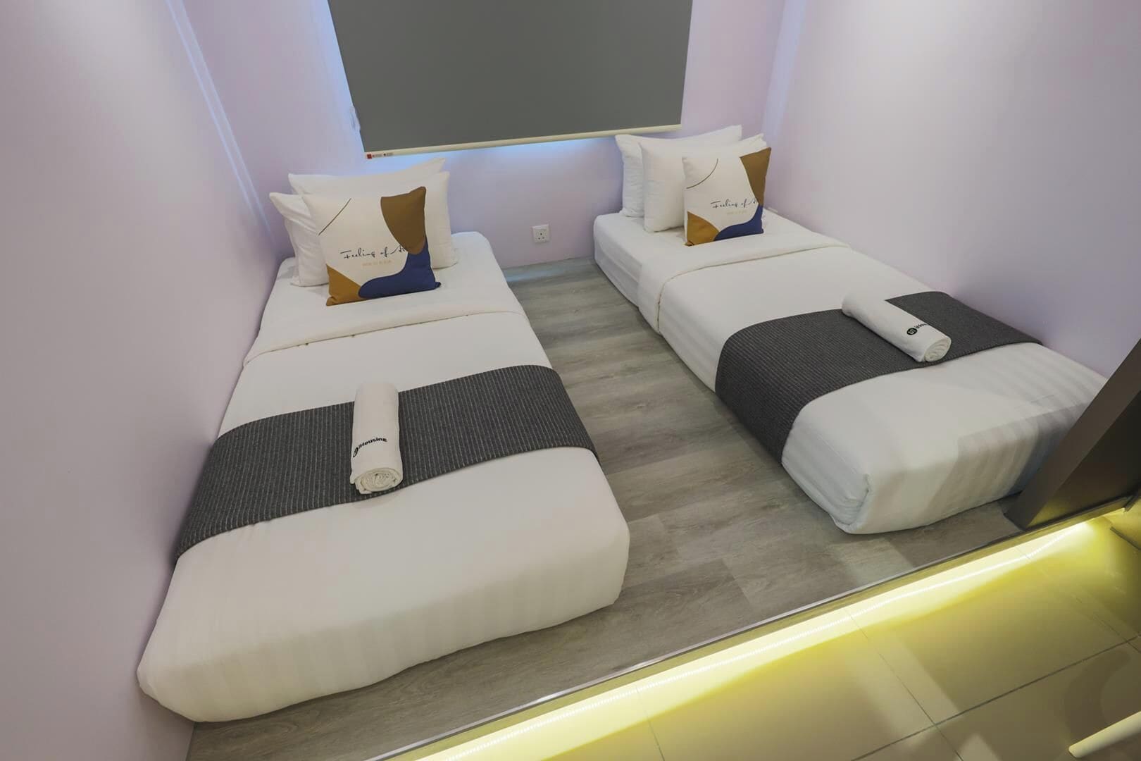 Habitación de hotel con dos camas individuales, cada una con una almohada y una toalla enrollada.