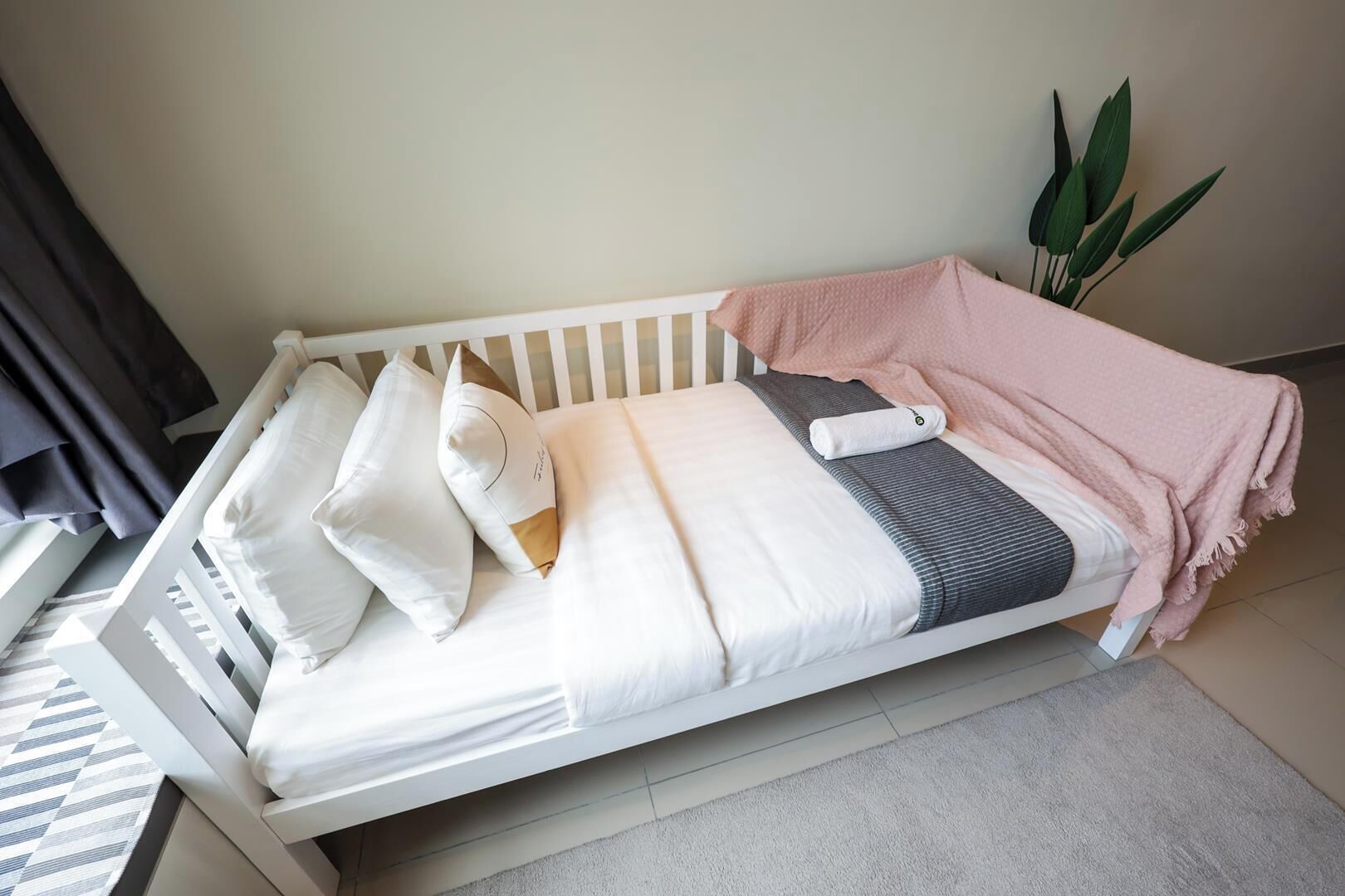 Una cama individual blanca con almohadas, una manta y una toalla doblada.