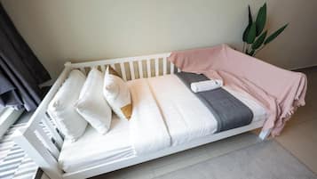 Una cama individual blanca con almohadas, una manta y una toalla doblada.