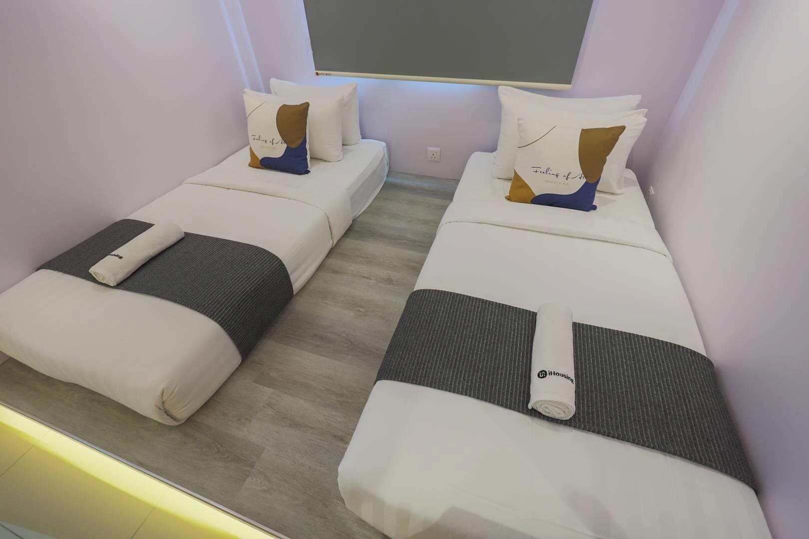 A hotel room with two single beds, each with a pillow and a blanket.