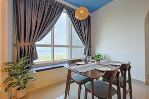 A dining area with a table set for two, a potted plant, and a view of the sea through large windows.