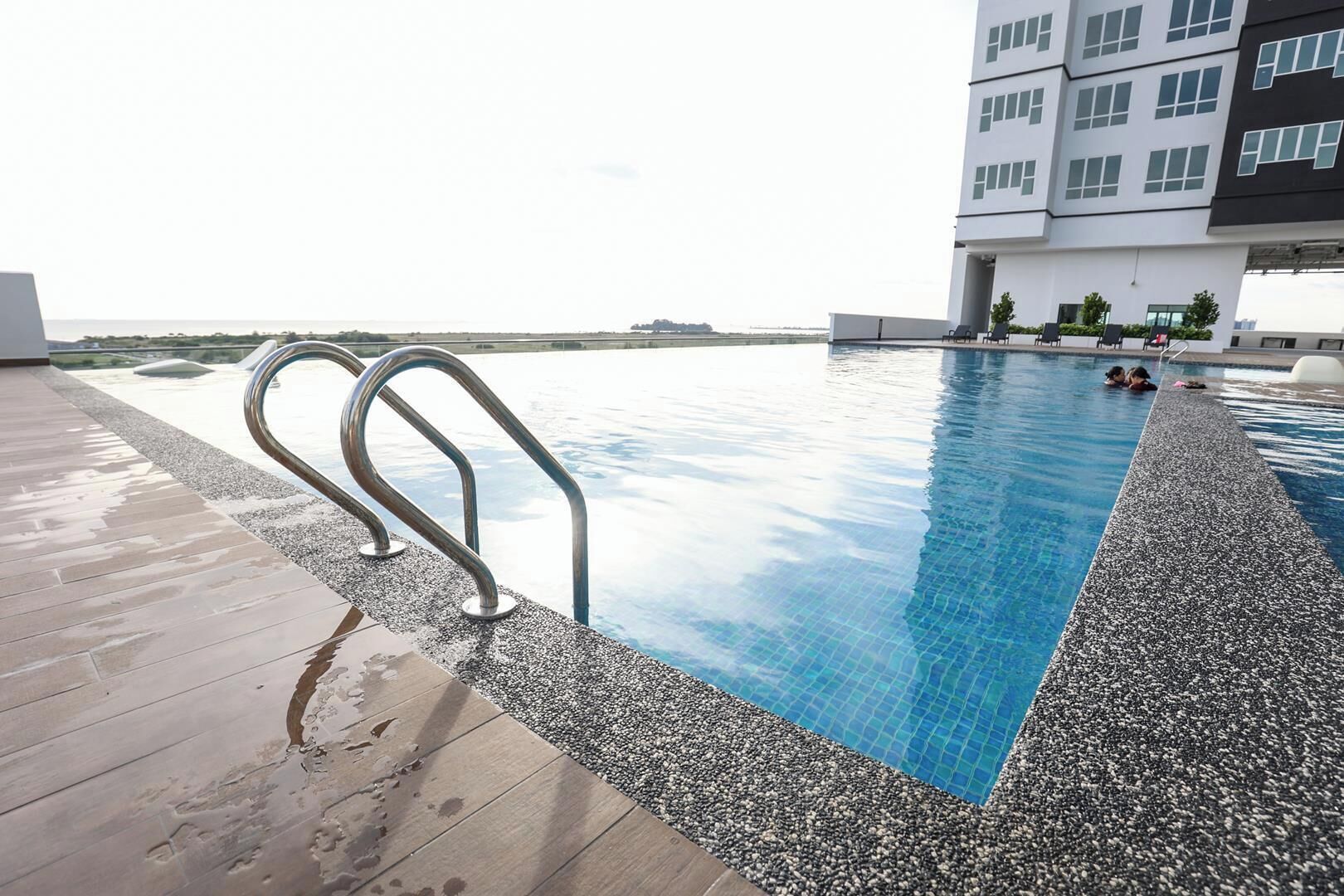 A swimming pool with a metal ladder, surrounded by a pebble border, and a wooden deck.