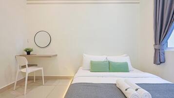 A hotel room with a bed, a desk with a chair, a small plant, and a window with curtains.