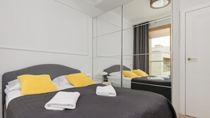 A modern bedroom with a large bed, a mirror, and a wardrobe.