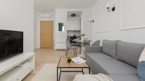 A modern living room with a flat-screen TV, grey sofa, and a small coffee table with a book and flowers.