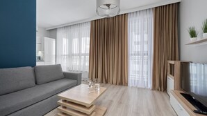 A modern living room with a grey sofa, a wooden coffee table, and a TV stand with a flat-screen TV. - Apartment with River View | Balcony and Parking (Wrocław)