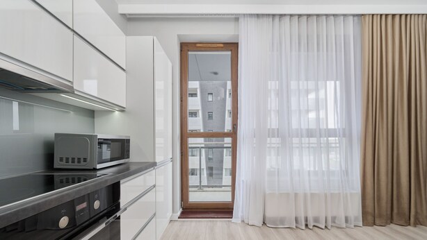 A modern kitchen with a microwave, a black countertop, and a wooden door leading to a balcony. - Apartment with River View | Balcony and Parking (Wrocław)