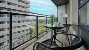 A balcony with a view of a river and buildings, a glass table with chairs, and a potted plant. - Apartment with River View | Balcony and Parking (Wrocław)