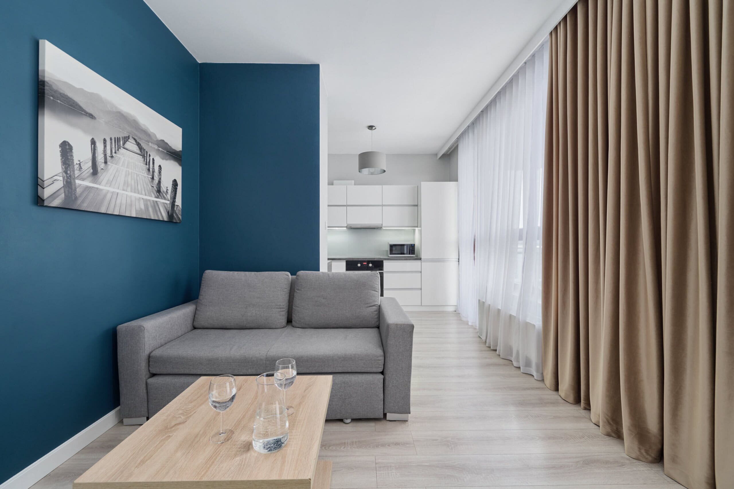 A stylish living room featuring a gray sofa, a wooden coffee table, and a striking blue accent wall, offering a modern and cozy vibe.
