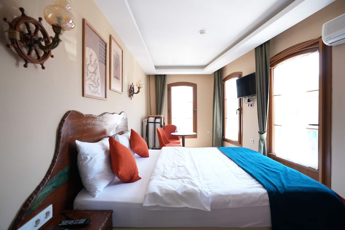 Habitación de hotel con una cama grande, un cabecero de madera, una mesita pequeña, una silla y un televisor instalado en la pared.