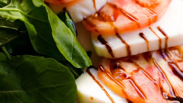 A plate of fresh mozzarella cheese slices topped with tomato and basil, drizzled with balsamic glaze. - Casta Diva Urla (Urla)