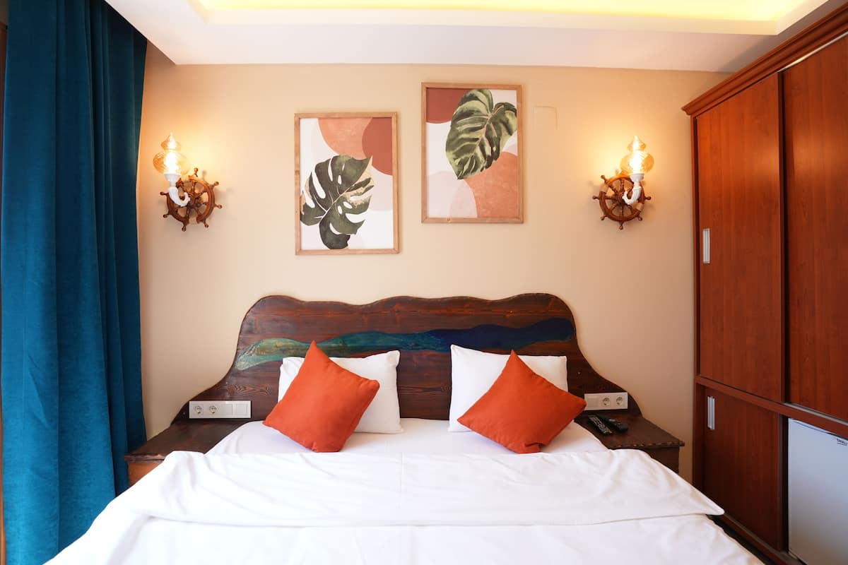 Una cama bien hecha con almohadas blancas y anaranjadas, un cabecero de madera y dos lámparas fijadas a la pared con diseños de timón.