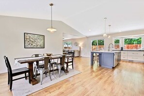 A spacious kitchen with a dining area, wooden flooring, pendant lighting, and a large window with a view of greenery. - Eagle Retreat • Fire Pit • Large Yard • Renovated (Eagle)