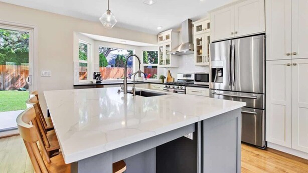 A modern kitchen with a large island, stainless steel appliances, and white cabinetry.