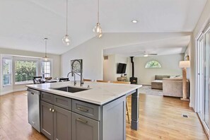 A spacious kitchen with a large island, modern pendant lights, and a view of a living area with a fireplace. - Eagle Retreat • Fire Pit • Large Yard • Renovated (Eagle)