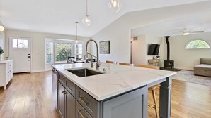 A modern kitchen with a large island, pendant lighting, and a fireplace in the living area.