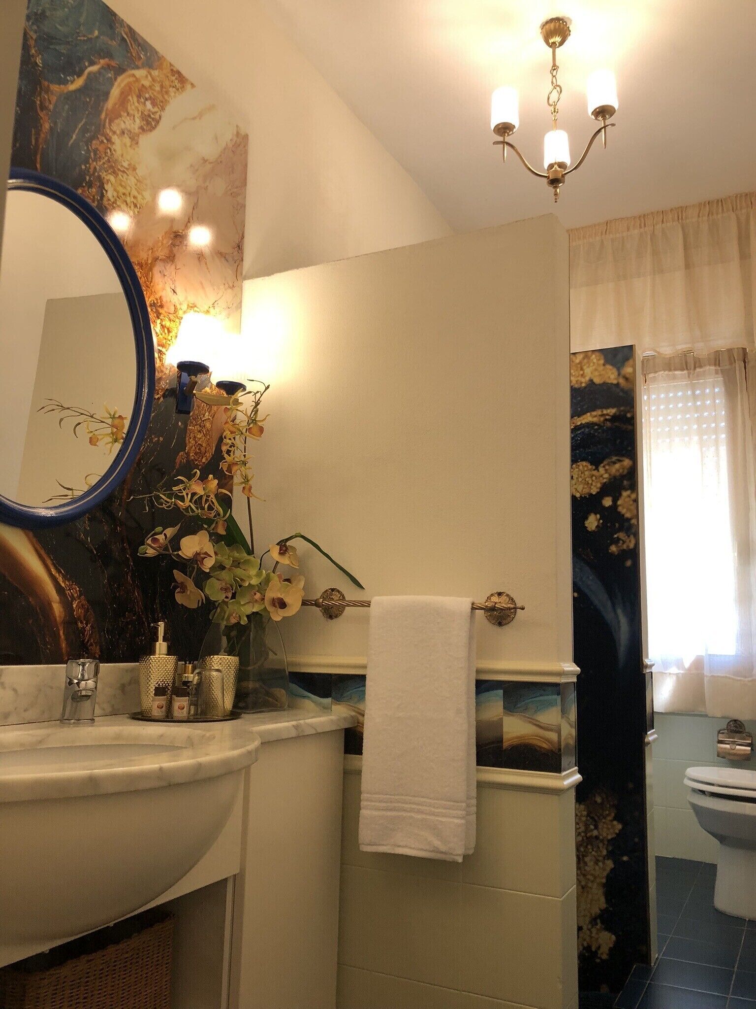 A bathroom with a marble sink, a large mirror, a chandelier, and a toilet.