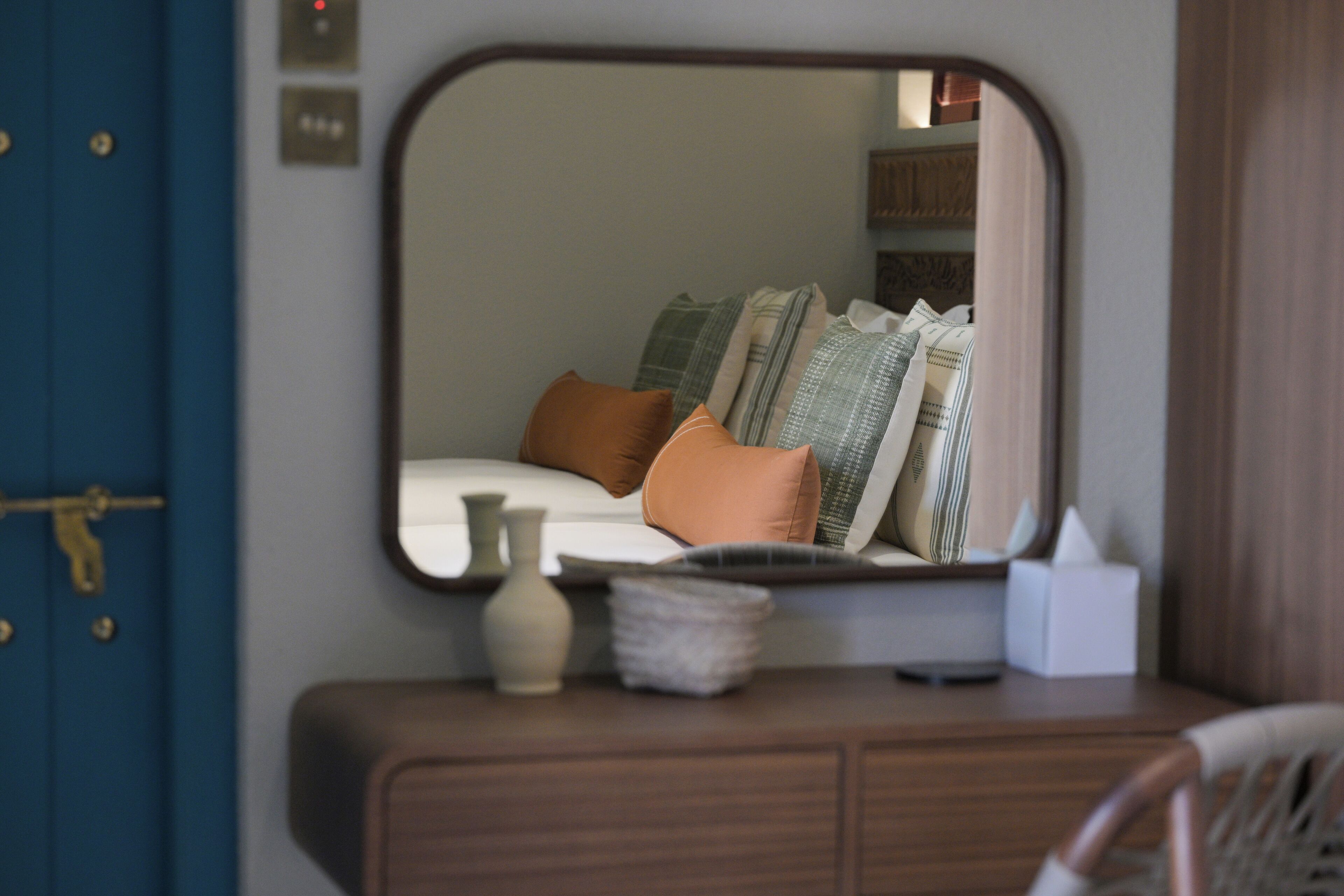 A bedroom with a bed, pillows, a dresser, and a mirror reflecting the room.