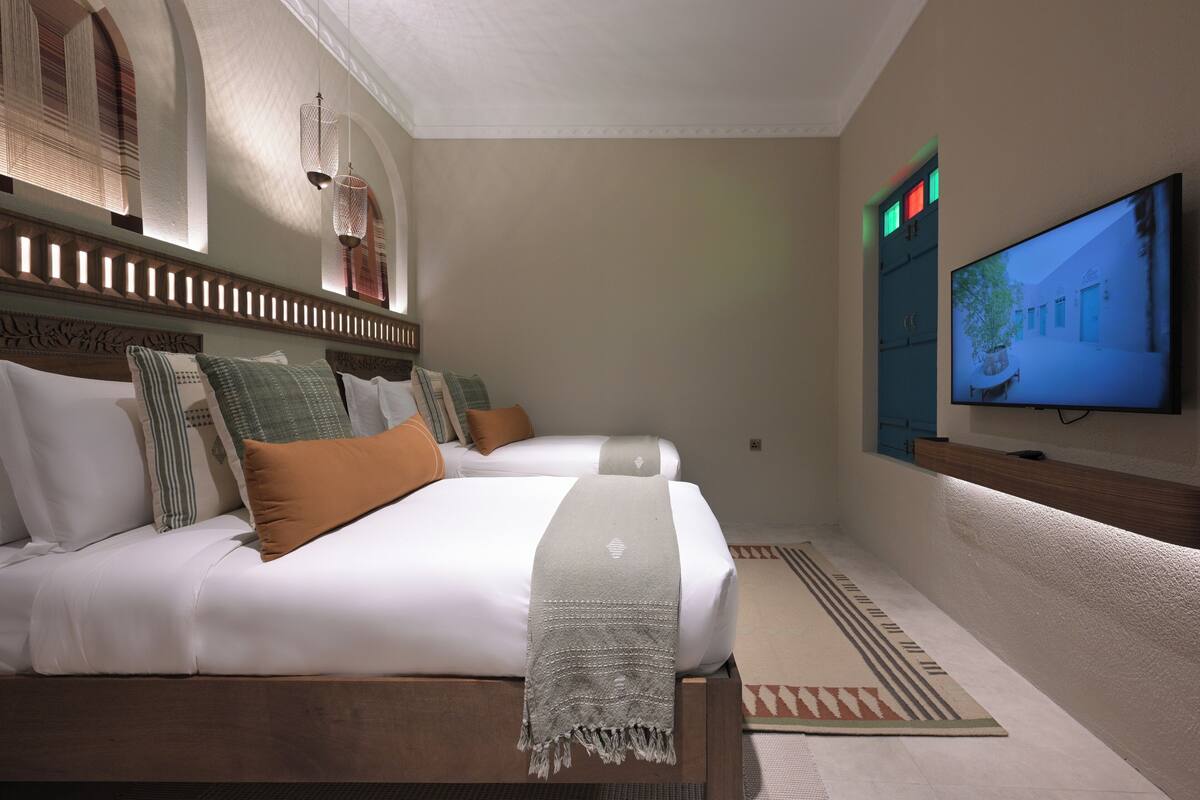 A hotel room with two beds, a television, and a patterned rug.