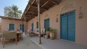A covered outdoor seating area with wooden furniture and blue doors. - NOZOL ALRAYAHEEN  (Khor Fakkan)