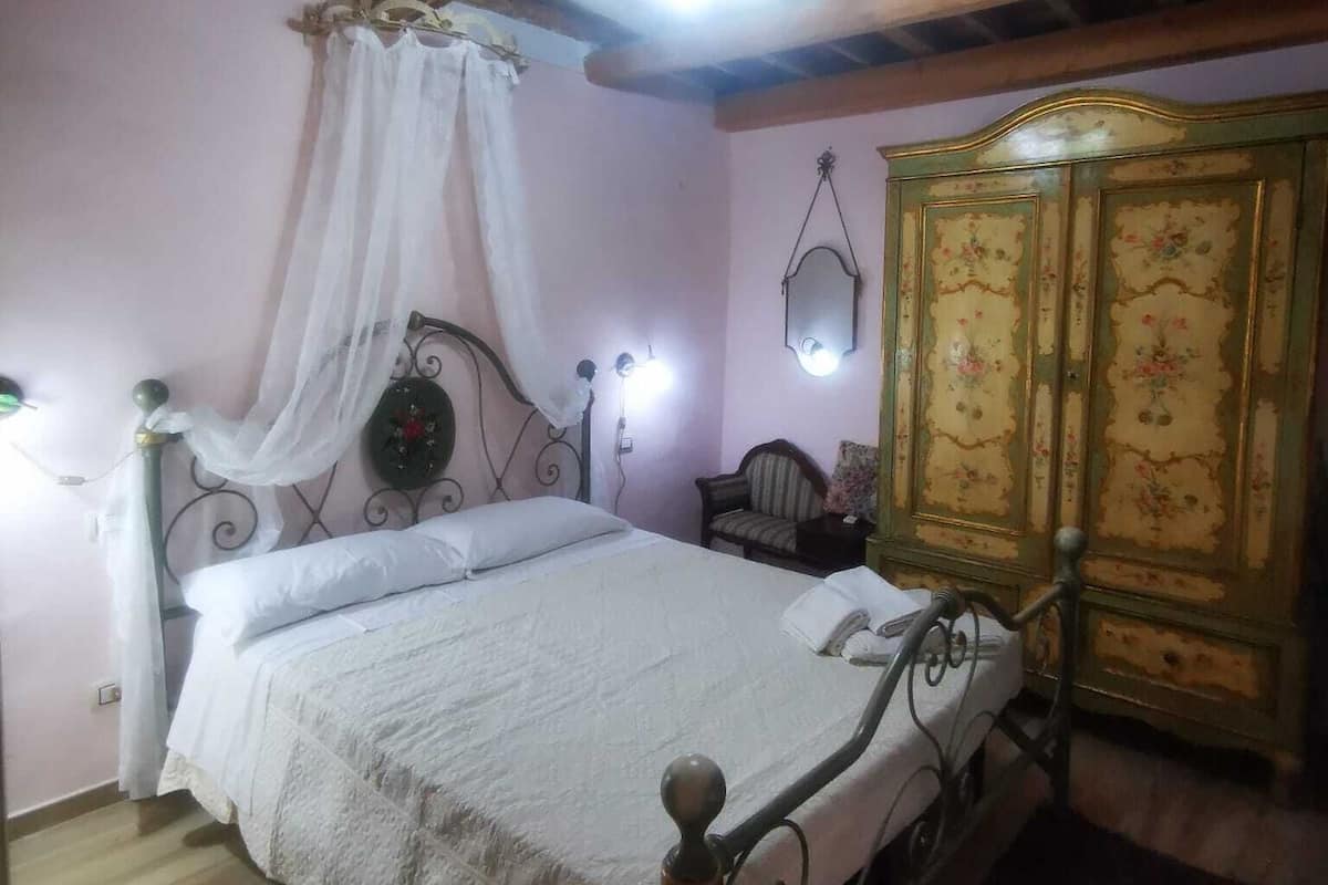A bedroom with a wooden ceiling, a bed with a canopy, a nightstand, a mirror, and a green cabinet.