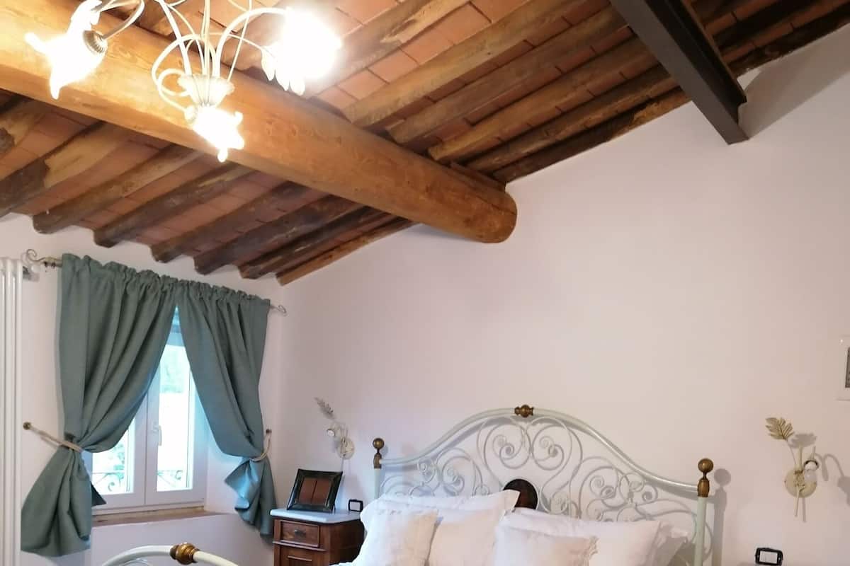 A bedroom with a bed, a chair, a nightstand, and a window with curtains.