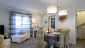 A modern living room with a sofa, dining table, and chairs. There is a TV, a lamp, and a clock on the wall.