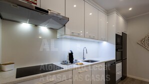 A modern kitchen with white cabinets, a stainless steel range hood, a coffee maker, and a sink.