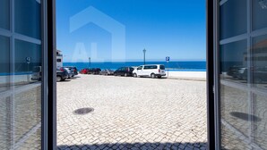 A view from inside a building looking out to a parking area with a beach in the background.