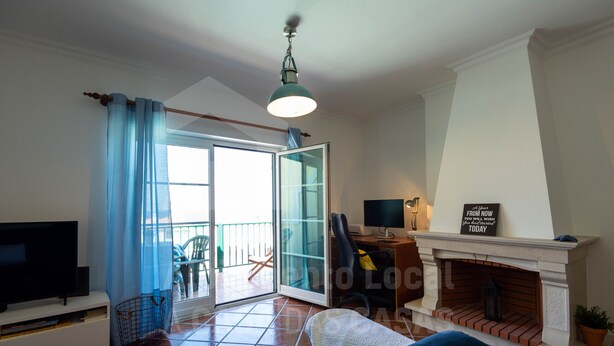 Ein Wohnzimmer mit Fernseher, einer Couch, einem Kamin und einer Schiebetür, die auf einen Balkon führt.