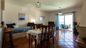 Ein Zimmer mit einem Bett, einem Esstisch mit Stühlen, einem Balkon mit Sitzgelegenheiten und einem Fernseher.
