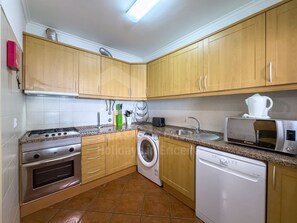 A kitchen with wooden cabinets, a stove, a microwave, a sink, and a washing machine. - Sunset Apartment by ACasaDasCasas (Ericeira)