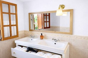 Une salle de bain avec un double lavabo, un miroir avec un luminaire et un porte-serviettes avec des serviettes blanches.
