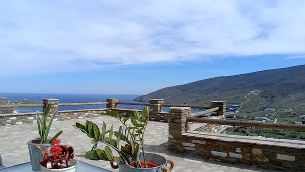 Eine Terrasse mit Topfpflanzen und Steinbrüstung mit Blick auf eine Küstenlandschaft.