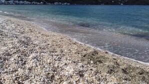 Ein Kiesstrand mit klarem Wasser und einem Berg im Hintergrund.