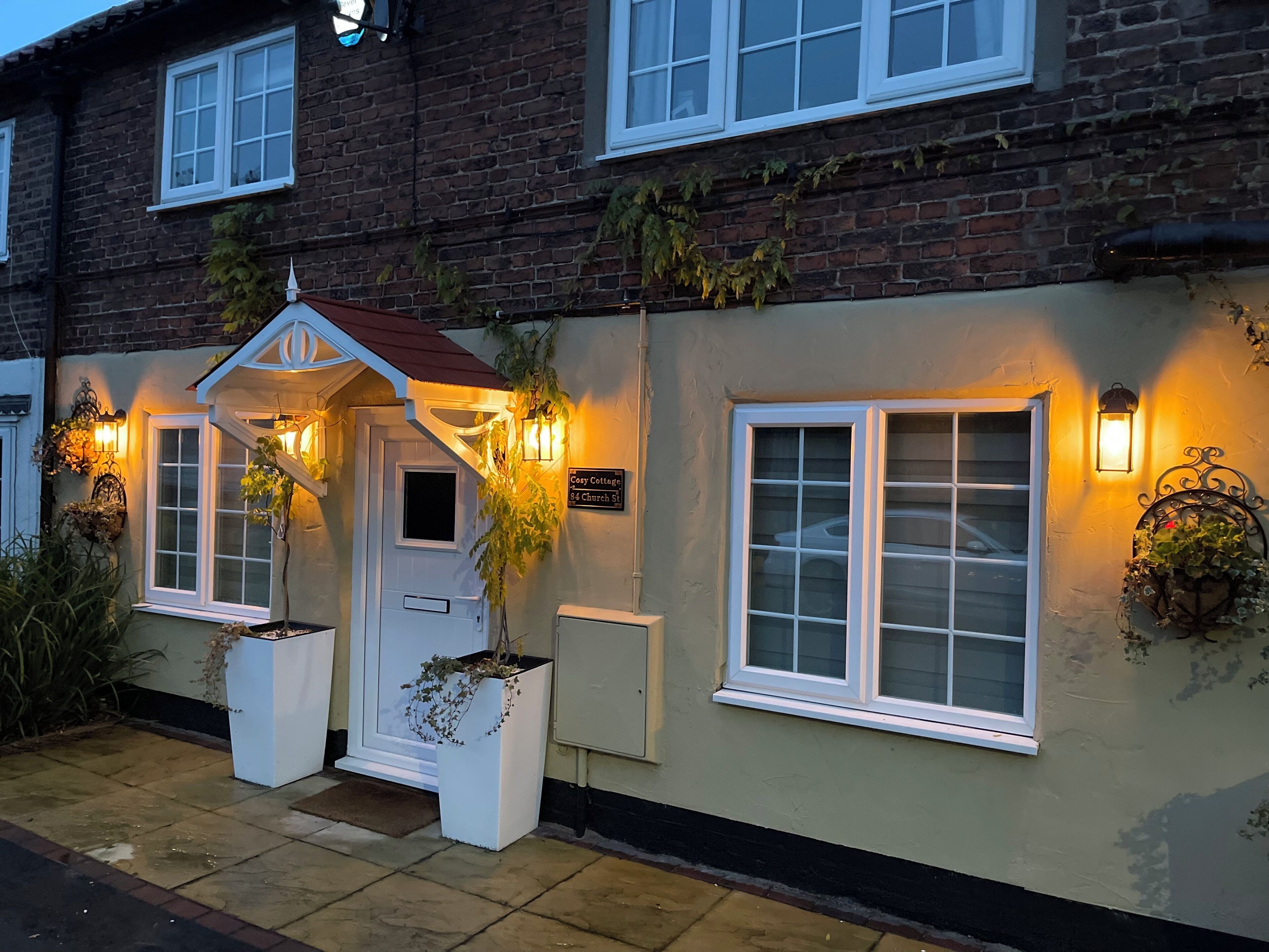 Un edificio con entrada blanca, un letrero que dice 'Cory Cottage 54 Church St.' y dos macetas con plantas.