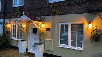 Un edificio con entrada blanca, un letrero que dice 'Cory Cottage 54 Church St.' y dos macetas con plantas.