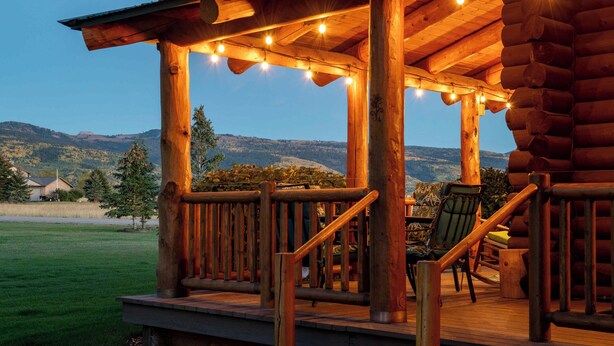 Una terraza de madera con vistas a montañas, una silla y una mesa.