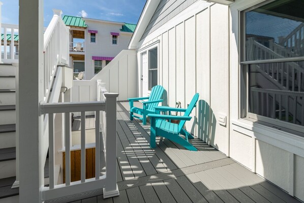 Una terraza de madera con barandilla blanca y sillas Adirondack turquesa.
