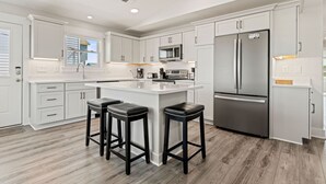 A modern kitchen with white cabinetry, a stainless steel refrigerator, and a central island with bar stools. - One More Moon 3 Bedroom Home in Kitty Hawk (Kitty Hawk)