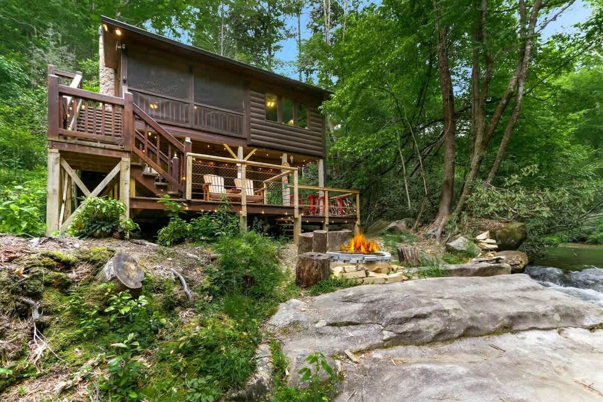 A cabin with a deck and outdoor seating, surrounded by forest.
