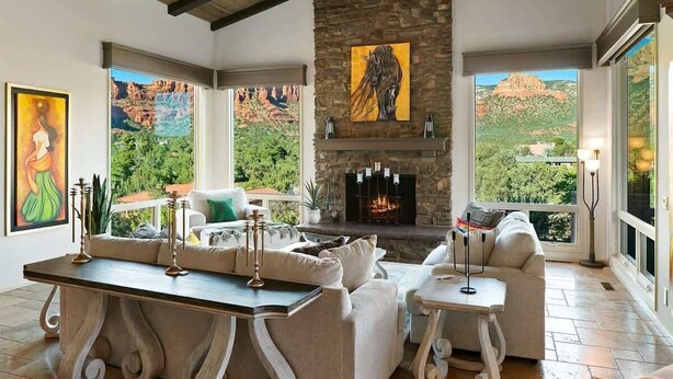 A spacious living room with a stone fireplace, large windows with mountain views, and modern furnishings.