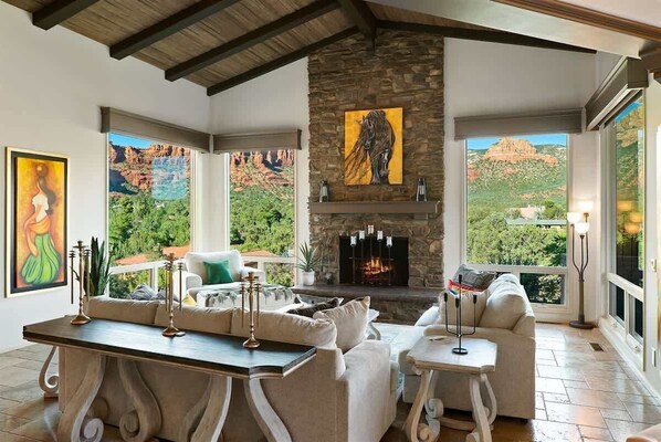 A spacious living room with a stone fireplace, large windows with mountain views, and modern furnishings.