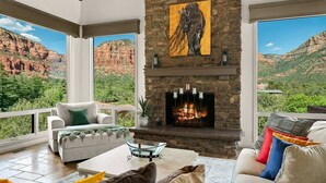 A living room with a stone fireplace, large windows, and a mountain view.