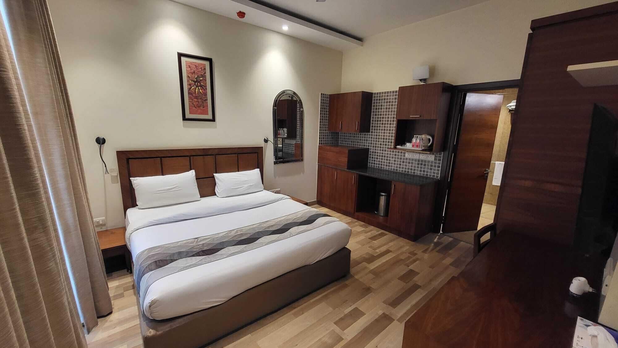 Ein Schlafzimmer mit Bett, Holz-Kopfteil, einer kleinen Küchenzeile und einer Tür zu einem weiteren Raum.